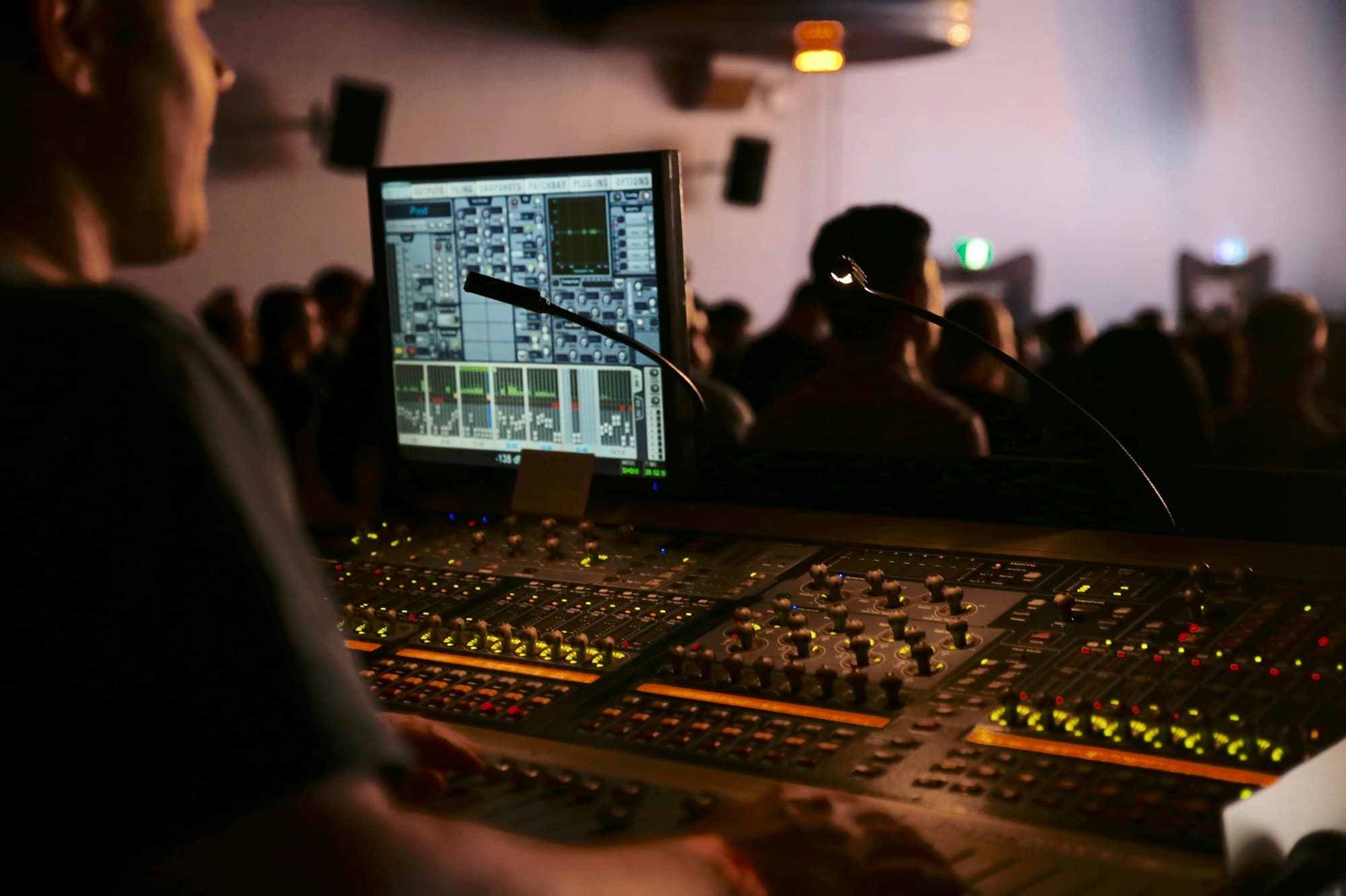 An engineer at a mixing desk during a live show, the crowd blurred behind the screen